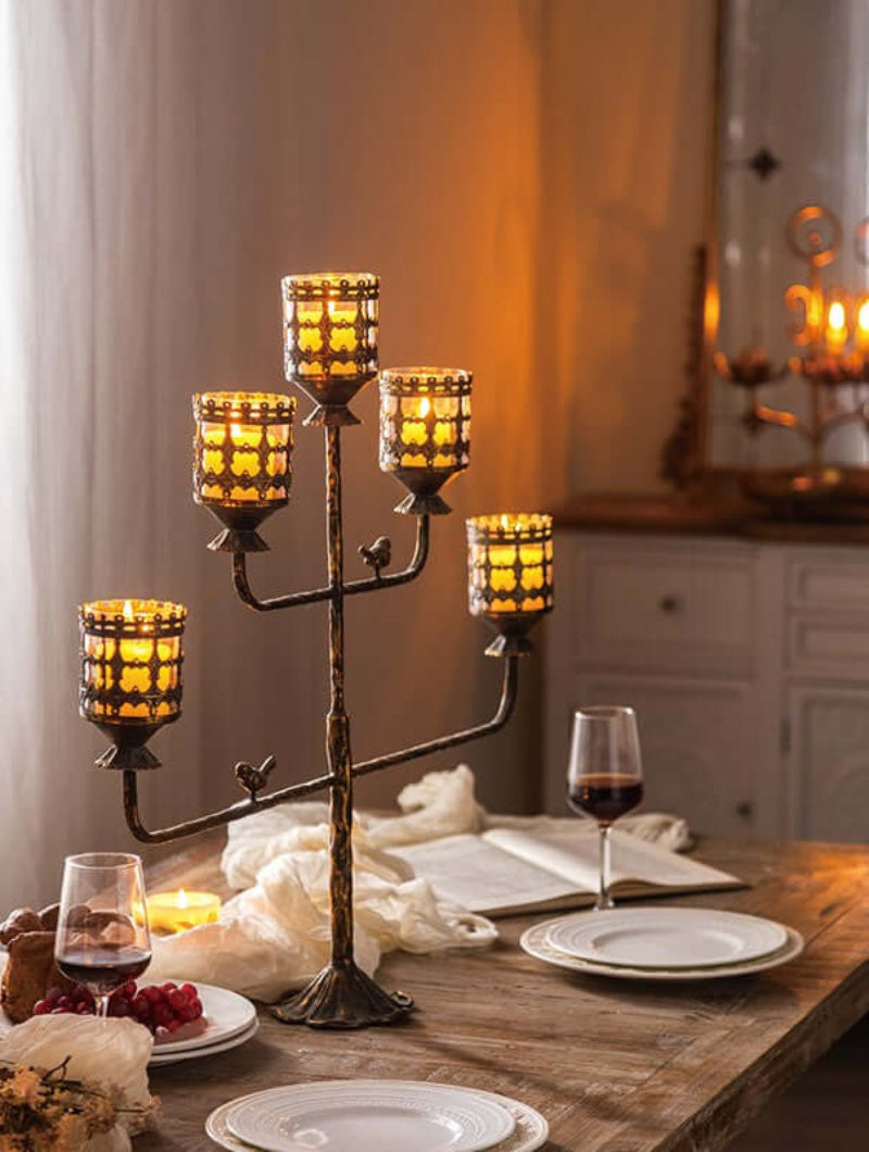 Antique amber glass votive candle holder centerpiece with glowing candles on a rustic dinner table setting.