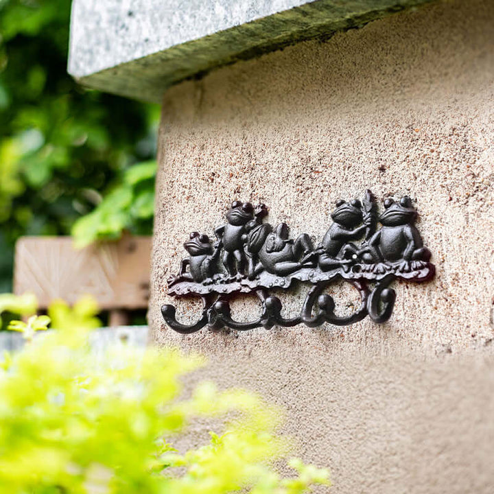 Decorative metal sculpture of frogs on a stone wall with greenery in the background