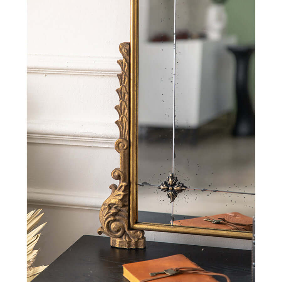 Close-up of vintage wall mirror with ornate gold frame and floral detail, reflecting elegant interior design.