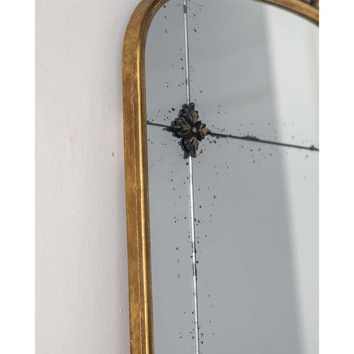 Close-up of vintage arched wall mirror with antique gold frame and floral detailing, reflecting elegance and craftsmanship.