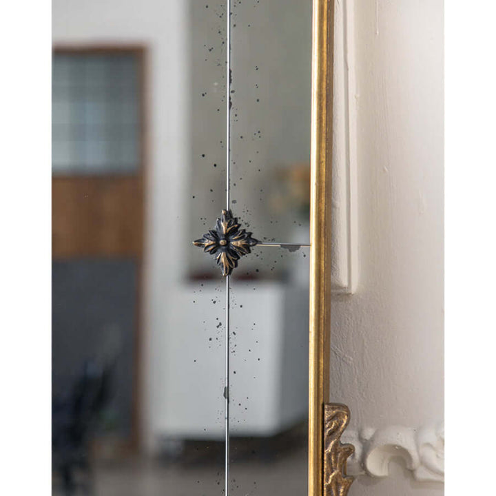 Close-up of vintage arched wall mirror with antique gold frame and floral detailing.