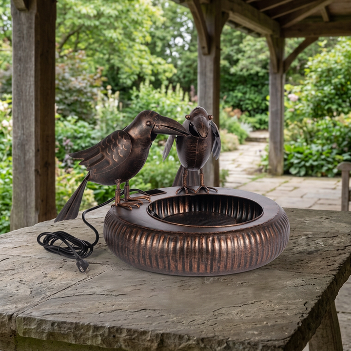 Black Bronze Chattering Crows Fountain staged unplugged on a stone table under a covered veranda with garden greenery beyond.