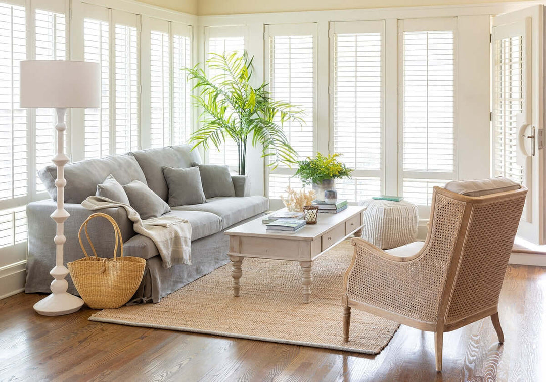 Living room with gray sofa, wicker chair, and large windows.