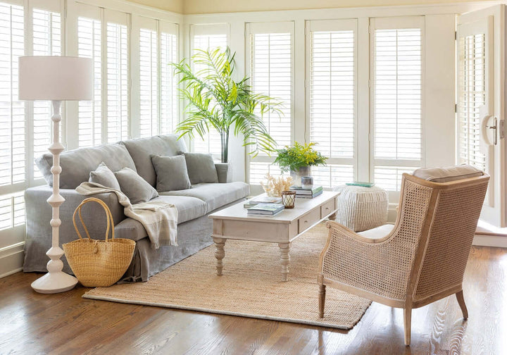 Living room with gray sofa, wicker chair, and large windows.