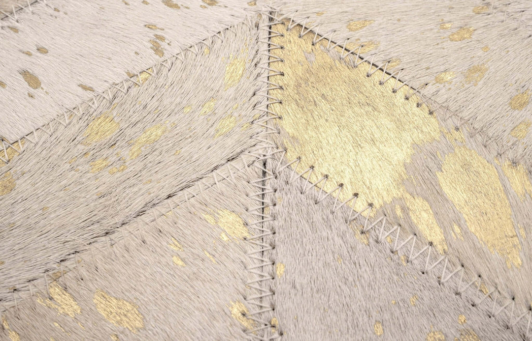 Close-up of a textured cowhide pillow with gold accents and stitching details.