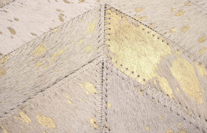Close-up of a textured cowhide pillow with gold accents and stitching details.
