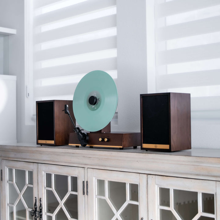 Record player with a green vinyl record on a wooden cabinet against a white wall.