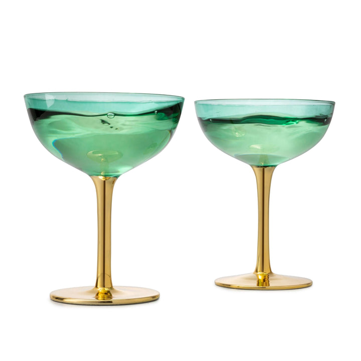 Two green cocktail glasses with gold stems on a white background
