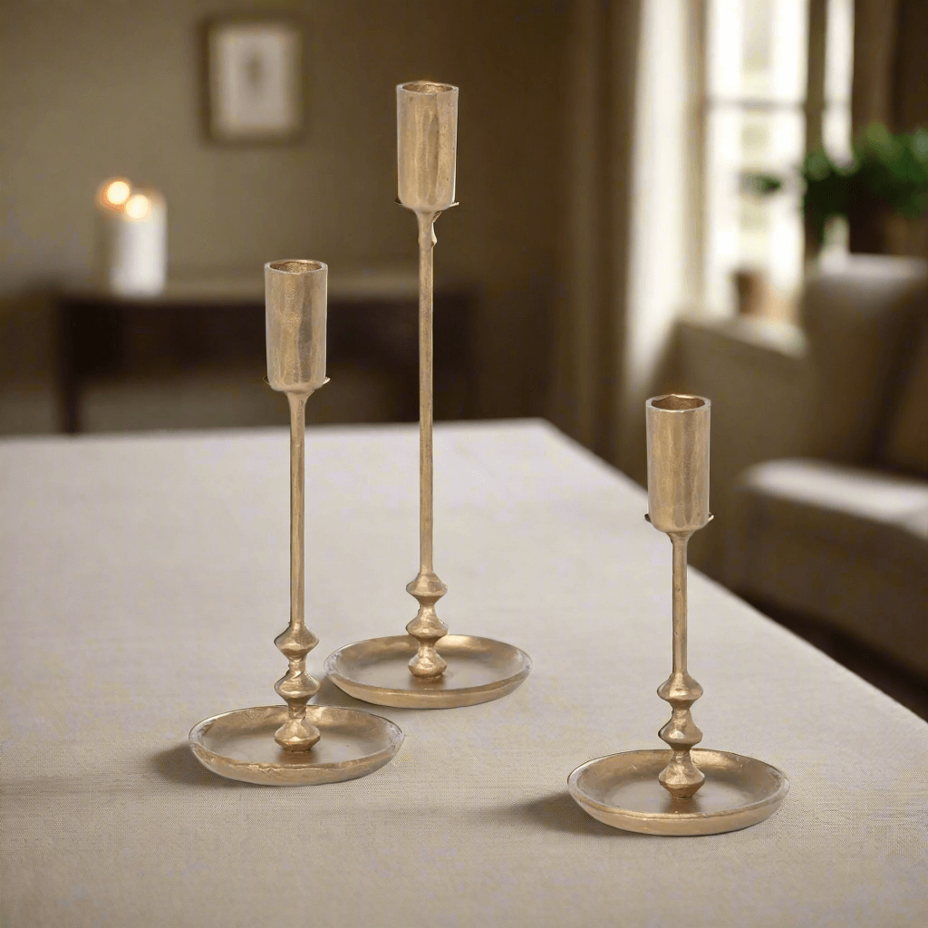 Set of vintage antique gold iron taper candle holders on table, three sizes, elegant design, ideal for home decor.