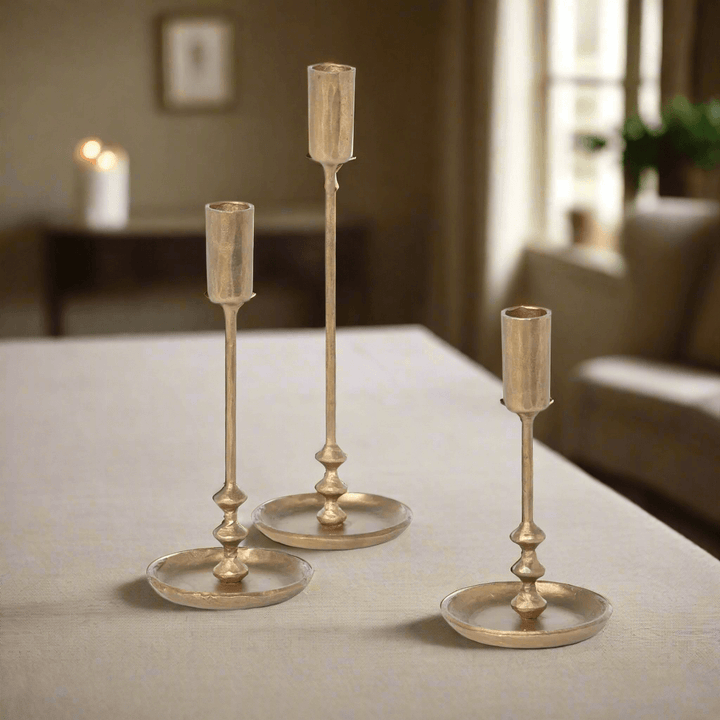 Set of vintage antique gold iron taper candle holders on table, three sizes, elegant design, ideal for home decor.