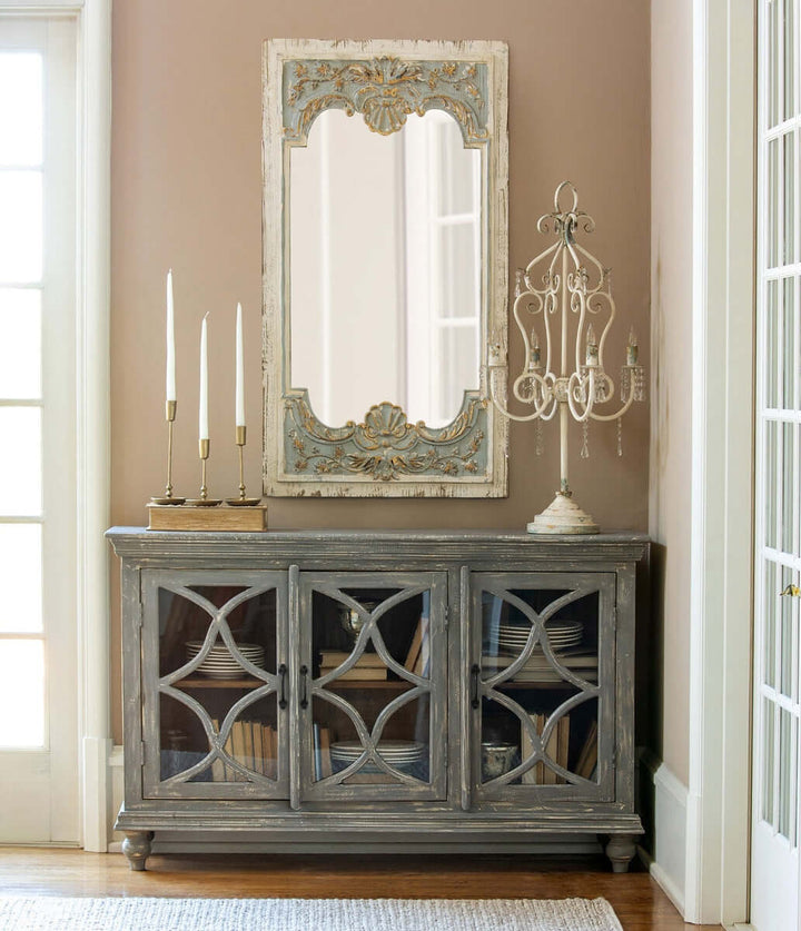 Vintage antique gold iron taper candle holders set on rustic cabinet with ornate mirror in elegant room.