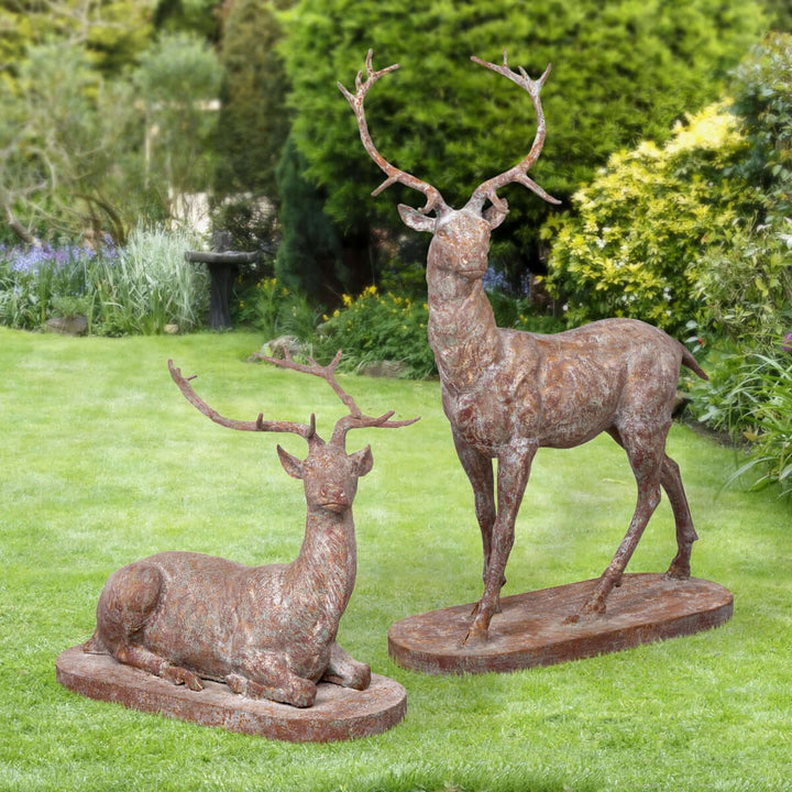 Antique style cast iron deer statues set in garden, featuring a standing stag and reclining deer, evoking a classic estate ambiance.