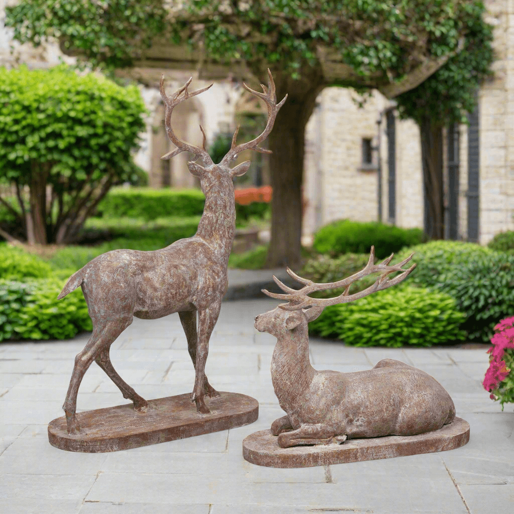 Antique style cast iron deer statues in a garden setting, featuring a standing stag and reclining doe, evokes English garden elegance.