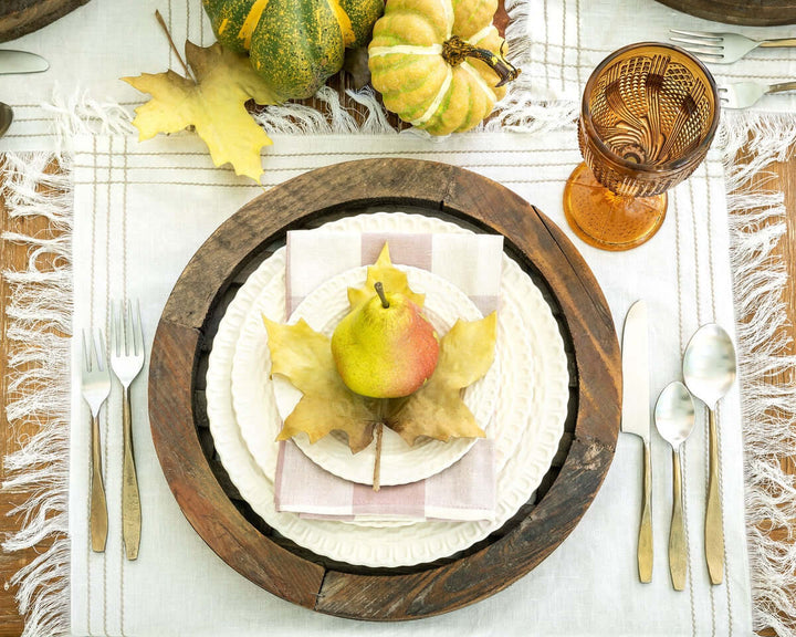 Elegant autumn table setting featuring hand-forged antique gold flatware, rustic wood charger, and decorative pear centerpiece.