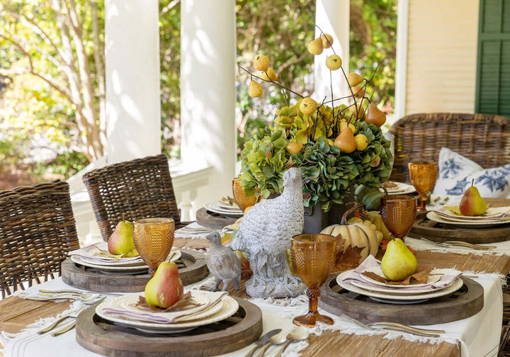 Elegant fall table setting with rustic wicker chairs, decorative pears and foliage centerpiece, amber glassware, and Hand-Forged Antique Gold Flatware Set.