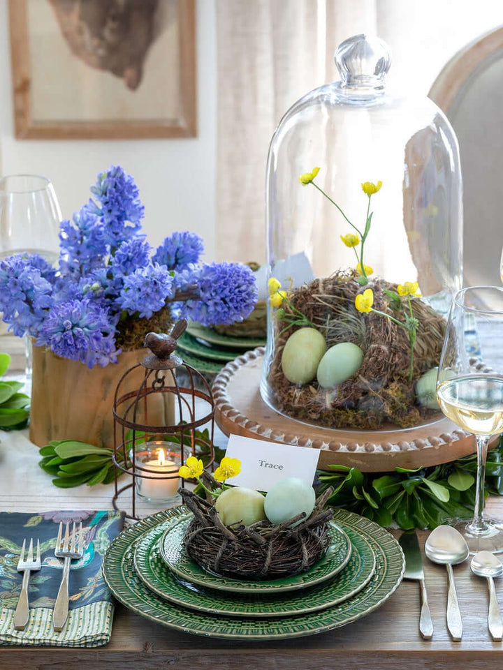 Elegant spring-themed table setting with floral centerpiece, decorative egg nest, and fine flatware, perfect for seasonal gatherings.