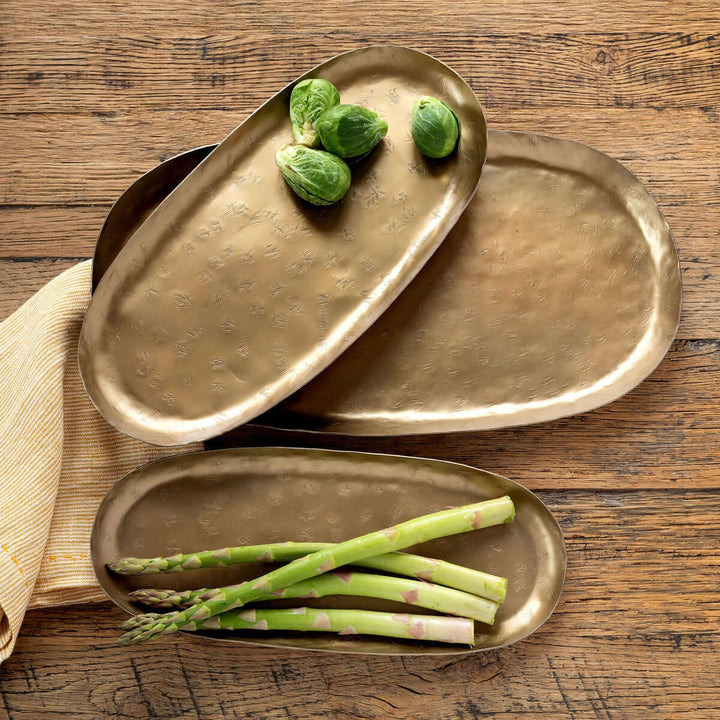 Vintage gold iron serving tray set with hand-hammered surfaces, showcasing asparagus and brussels sprouts on rustic wooden table.
