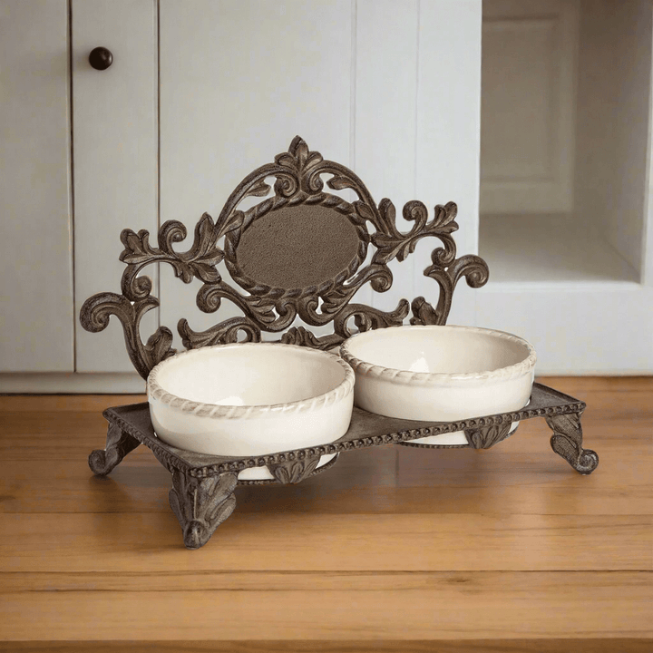 Ornate elevated pet feeder with vintage cast iron double bowl stand on wooden surface, featuring intricate European design.