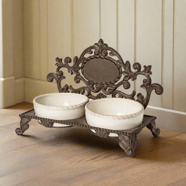 Ornate elevated pet feeder with vintage cast iron double bowl stand on wooden floor, elegant traditional European design.
