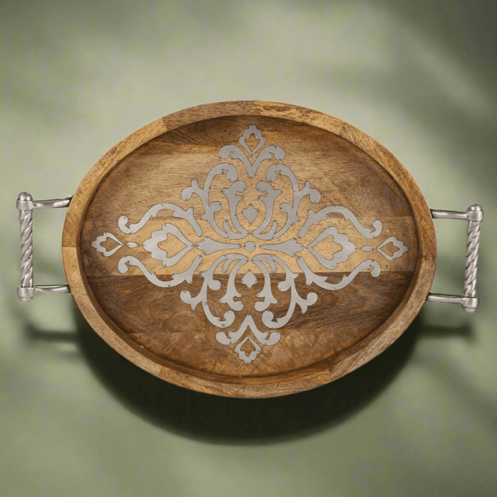 Rustic mango wood serving tray with intricate design and metal handles on green background.