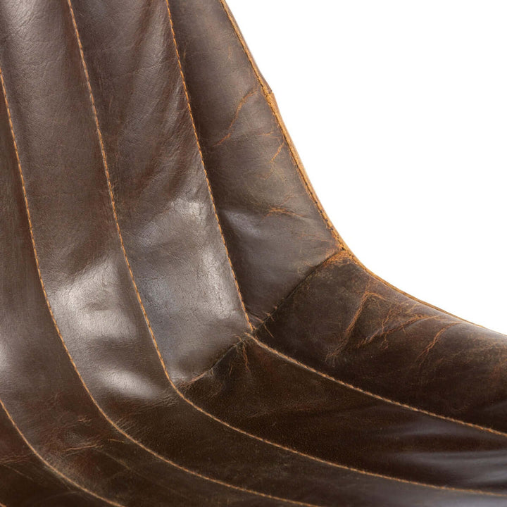 Close-up of vintage industrial desk chair with aged leather showing rich brown color and distressed texture.