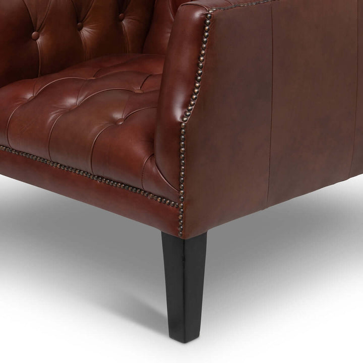 Close-up of cordovan brown tufted leather club chair with nailhead trim and dark wooden legs, showcasing luxury and classic design.