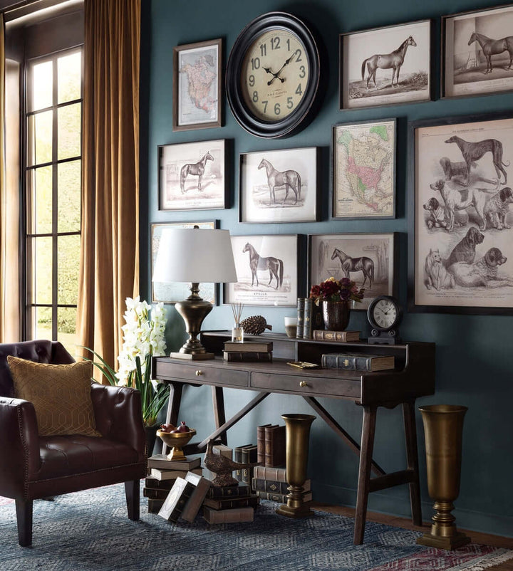 Vintage library room with a tufted leather club chair in cordovan brown, wooden desk, framed artwork, large clock, and books.