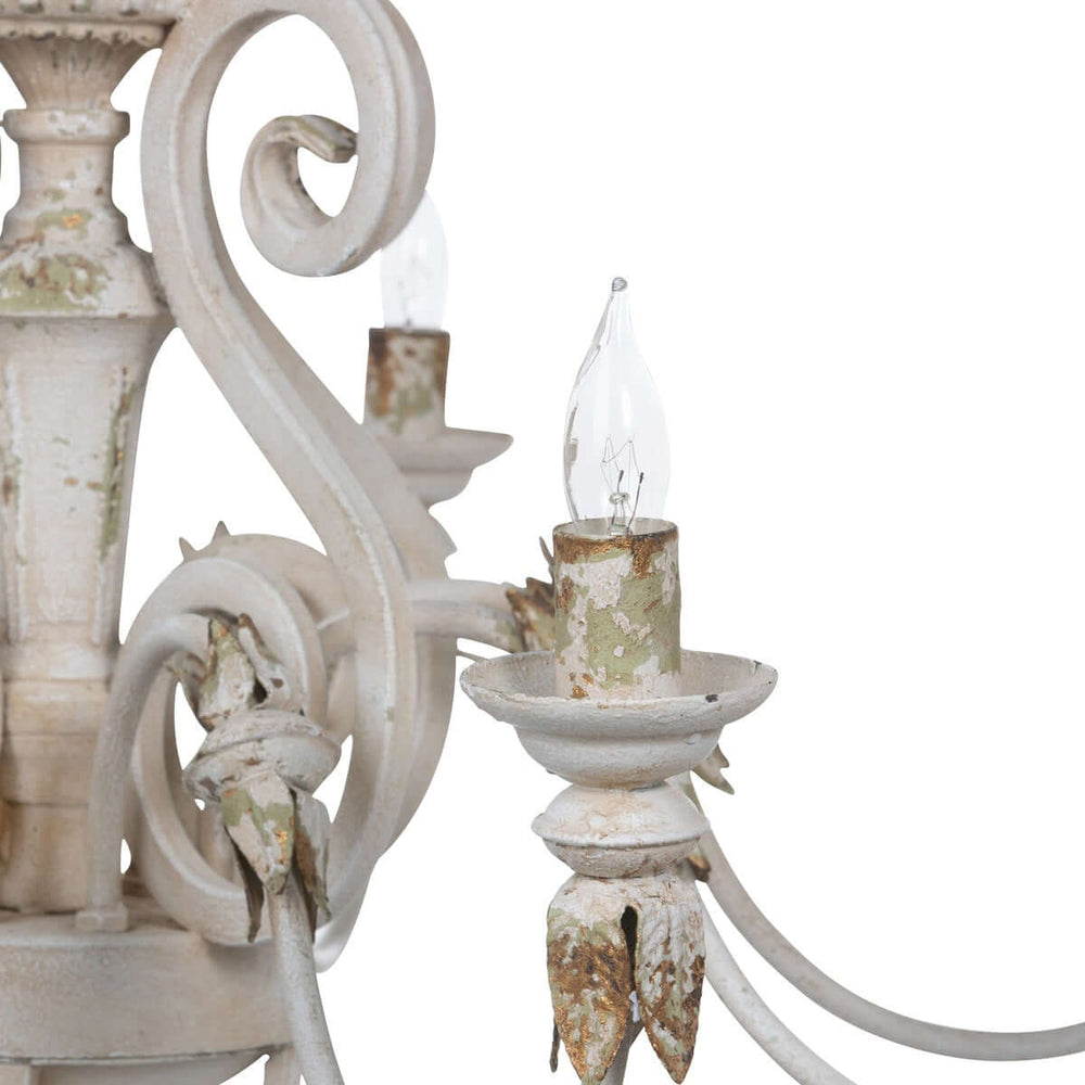 Close-up of rustic French country chandelier with gold leaf accents and distressed cream finish, evoking antique charm.