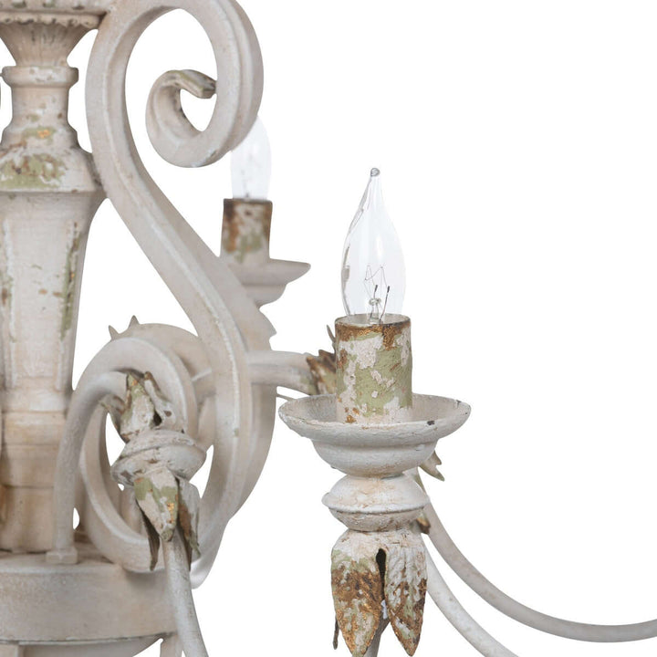 Close-up of rustic French country chandelier with gold leaf accents and distressed cream finish, evoking antique charm.