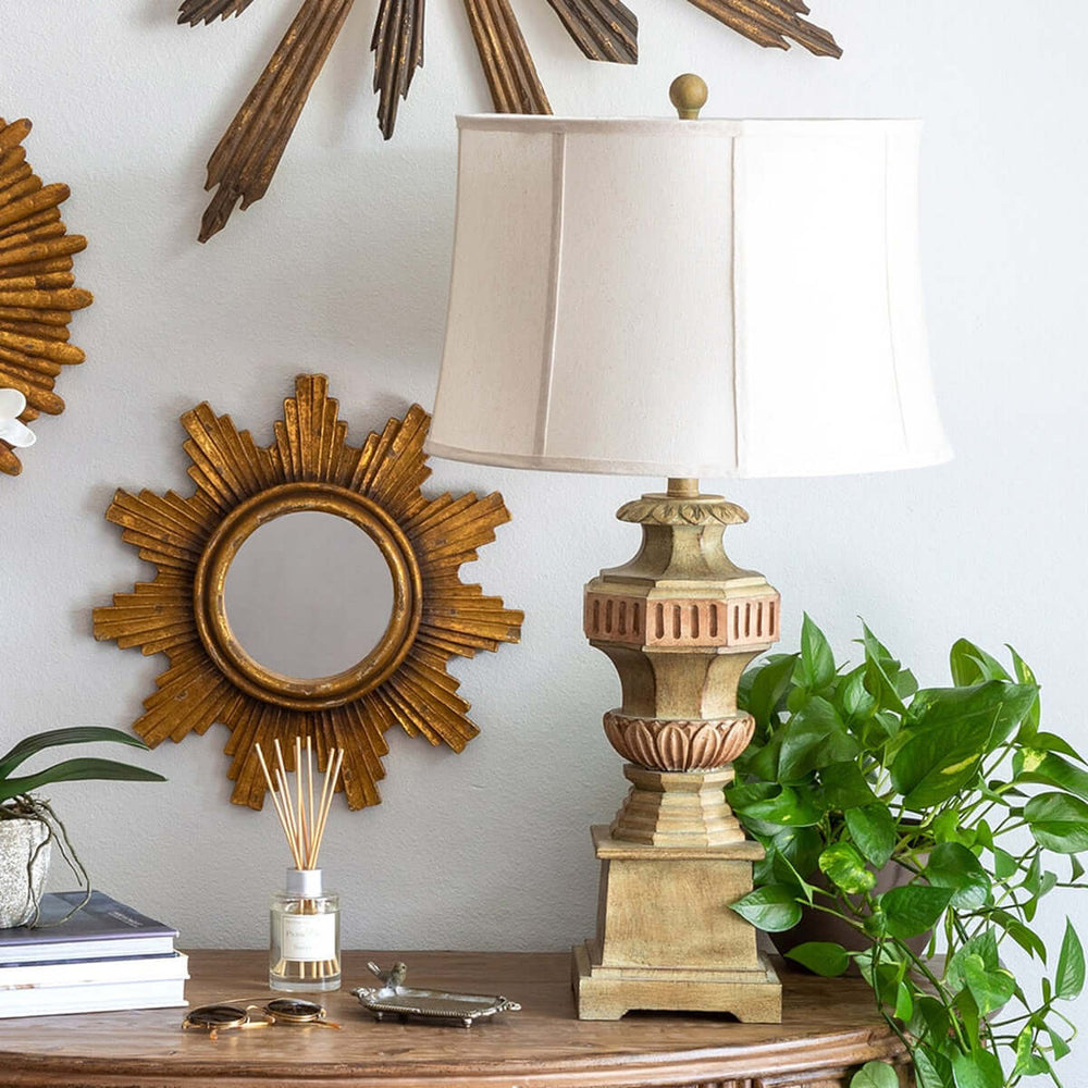 Vintage Greek Column Table Lamp on wooden table beside sunburst mirror and green plant