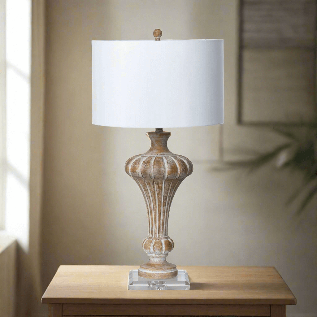 Vintage whitewashed urn table lamp with crystal base and linen shade on wooden table in softly lit room.