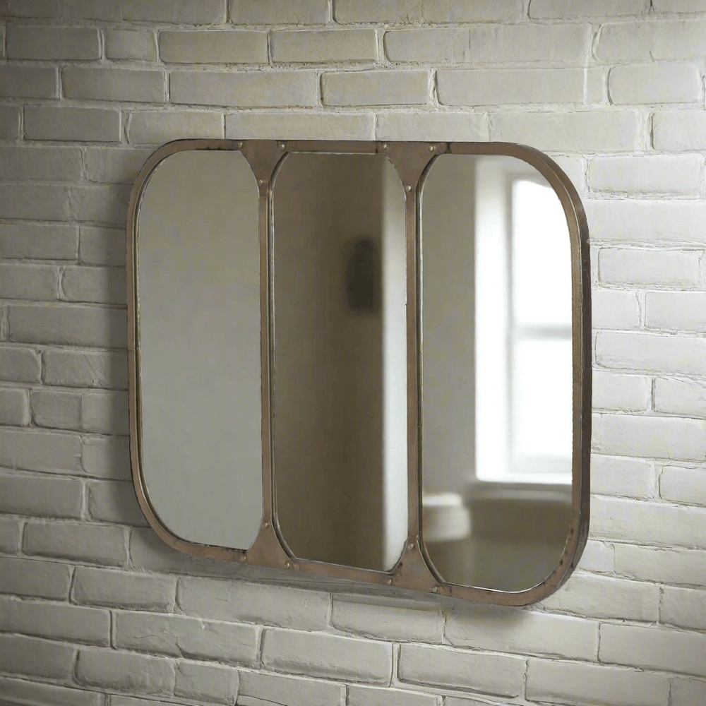 Vintage industrial wall mirror with aged brass metal frame, featuring arched corners and riveted iron construction, on a white brick wall.