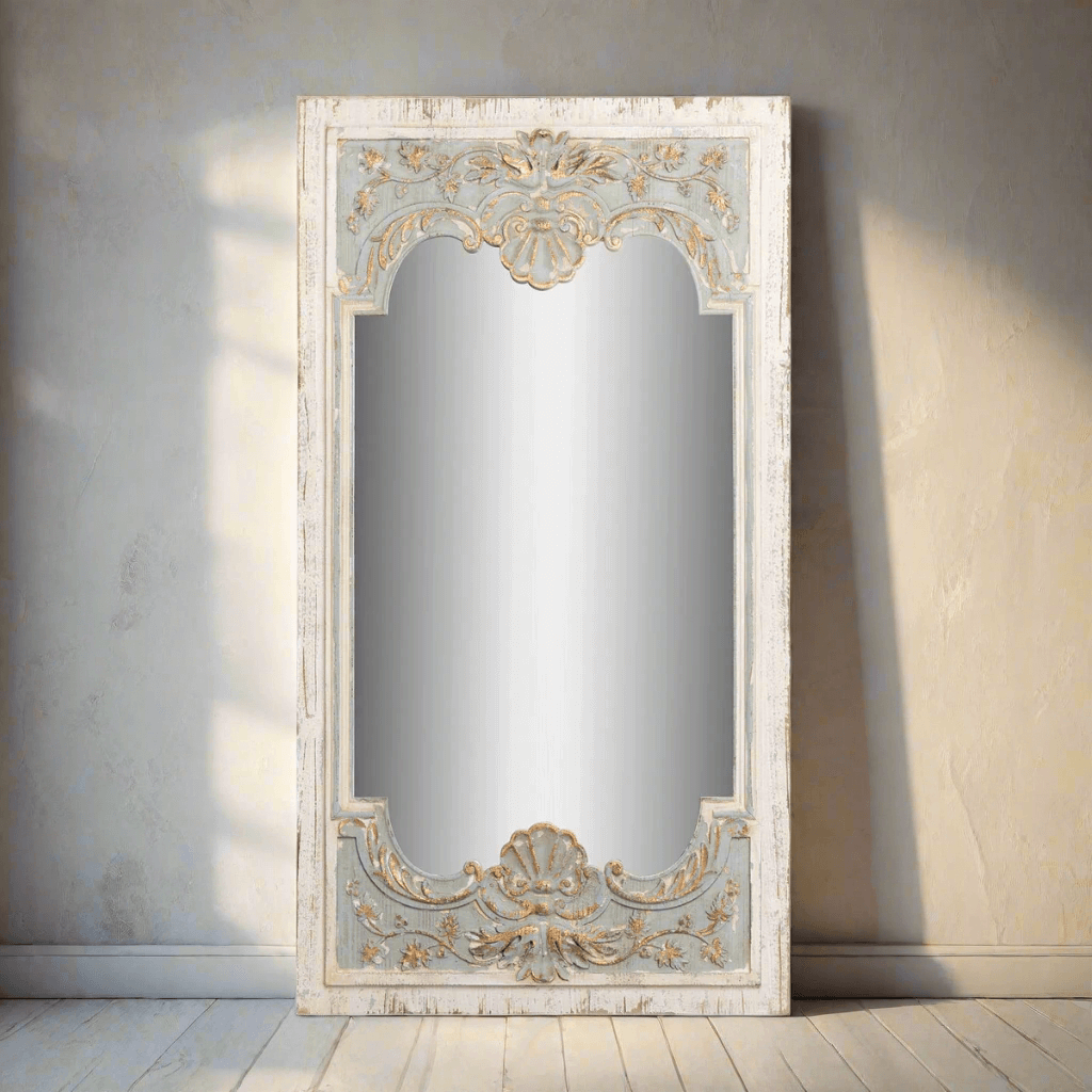 Vintage French country carved wood mirror with distressed blue frame, ornate shell design, and floral motifs on wall.