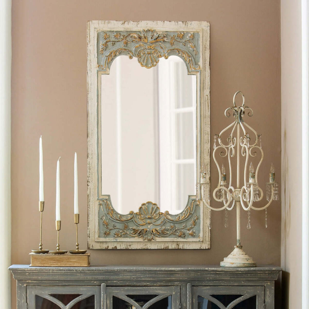 Vintage French country carved wood mirror with distressed blue frame, ornate shell and floral motifs, on a wall above a sideboard.