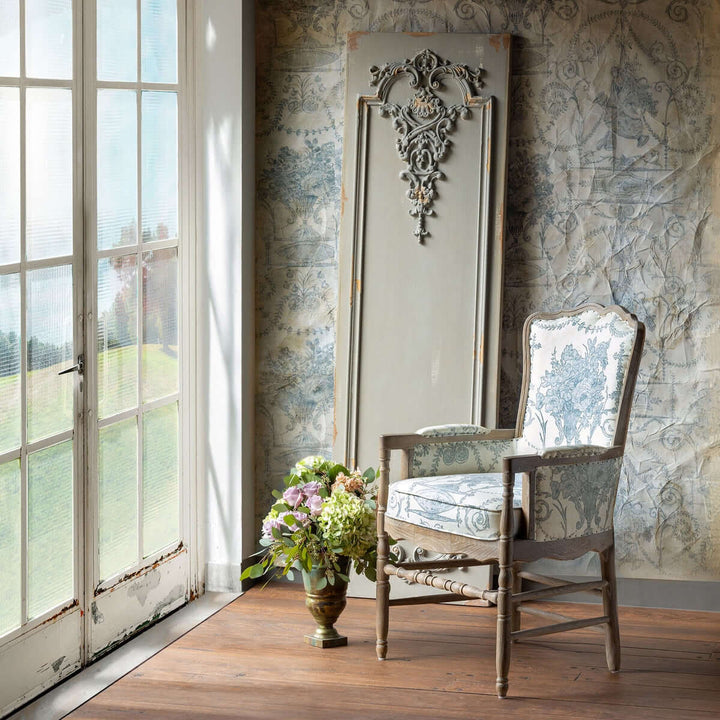 Distressed French wall panel in antique Art Nouveau decor with floral chair and vase by a window in a classic interior setting.