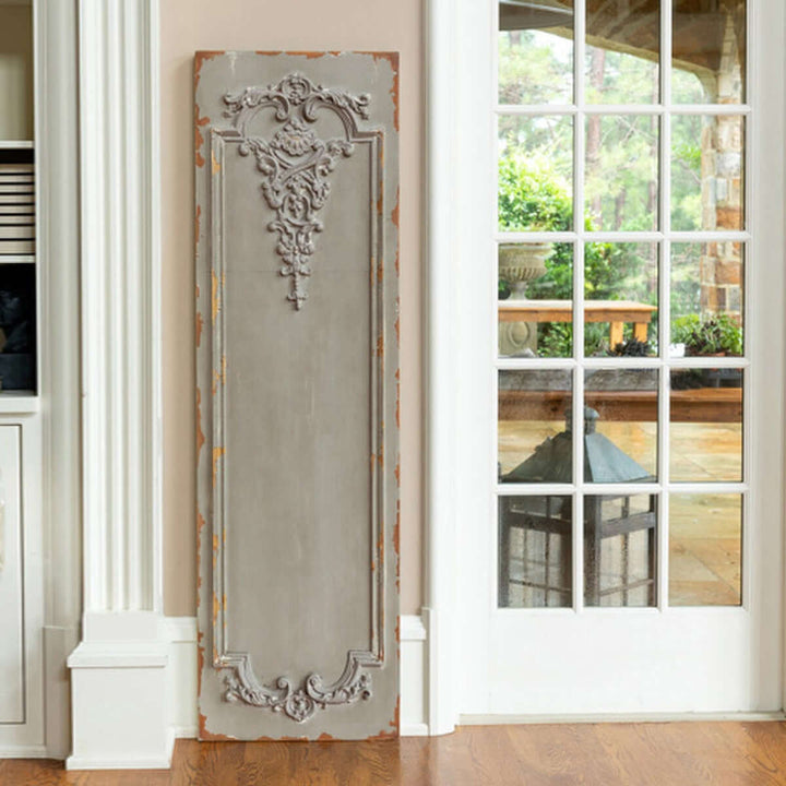 Distressed French wall panel with Art Nouveau decor in slate grey, featuring ornate scrollwork, leaning against a wall near a glass door.