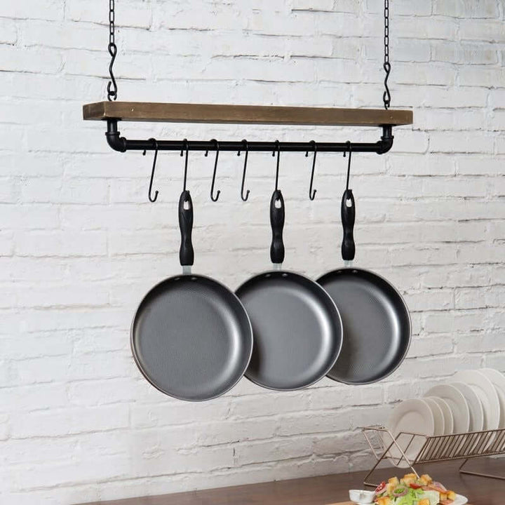 Hanging pot rack with four frying pans against a white brick wall.