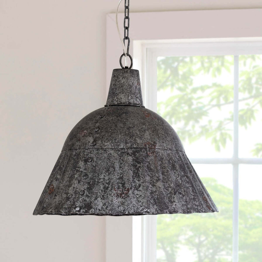 Vintage-style metal pendant light hanging in a room with a window in the background.