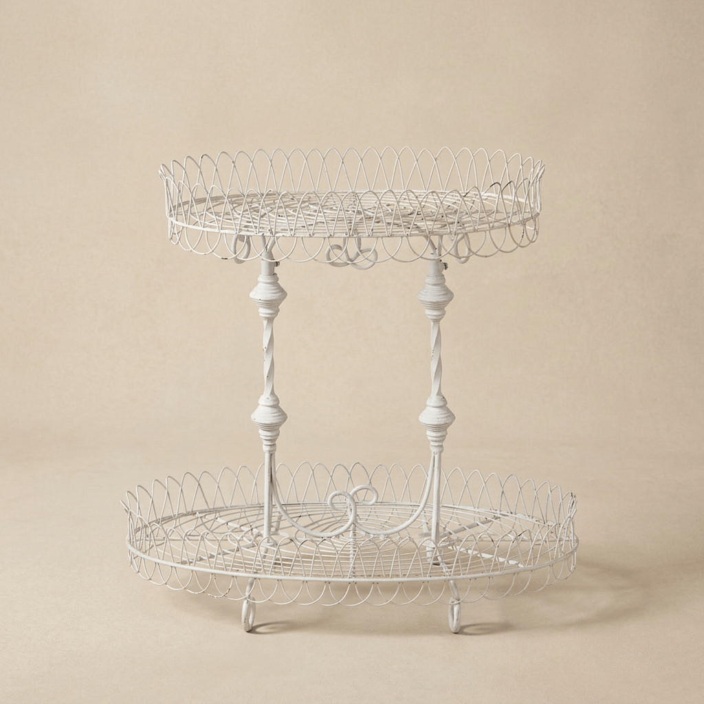 Fleury antiqued white iron plant stand with two oval wire shelves and decorative spindle supports against a warm beige background.