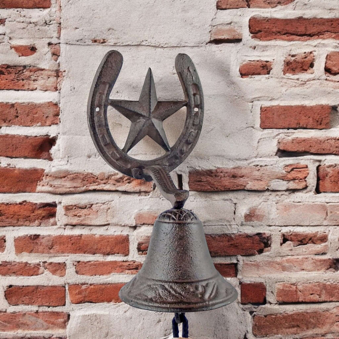 Decorative metal bell with horseshoe and star against a brick wall