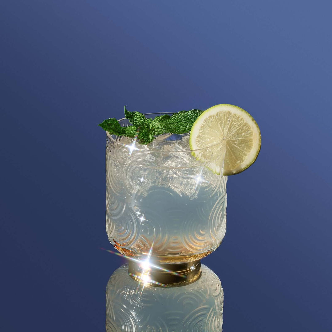 Cocktail with lime and mint on a reflective surface against a blue background