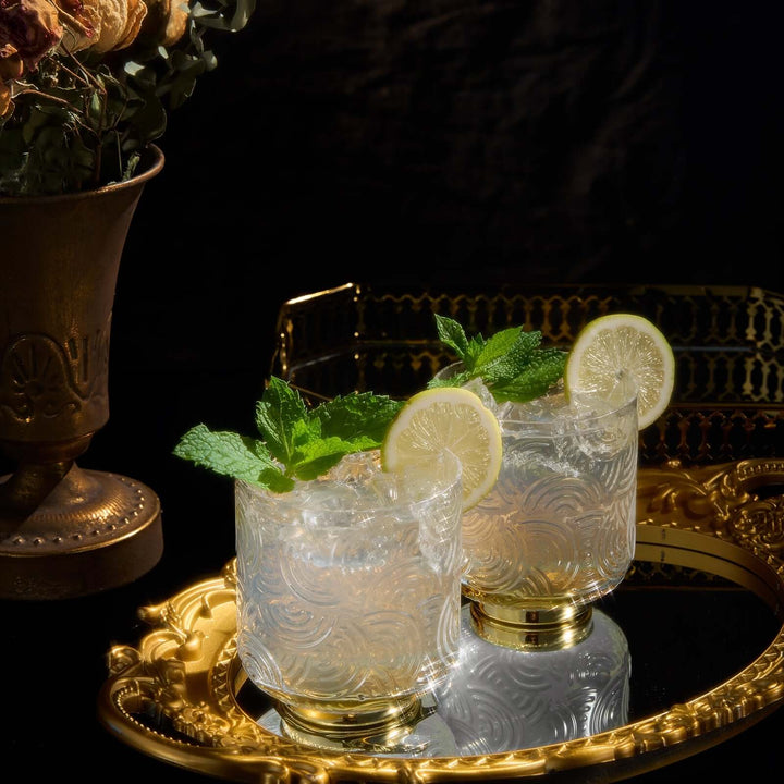Two cocktails with lemon slices and mint leaves on a gold tray with a dark background