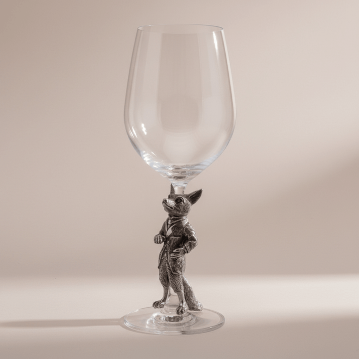 Clear wine glass with a silver fox figurine base on a beige background