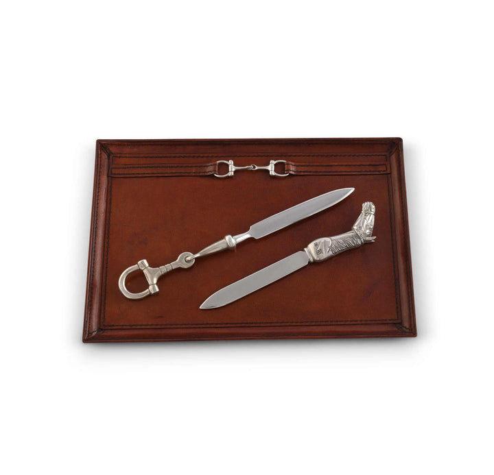Two silver letter openers with horsebit handles on a brown leather tray.