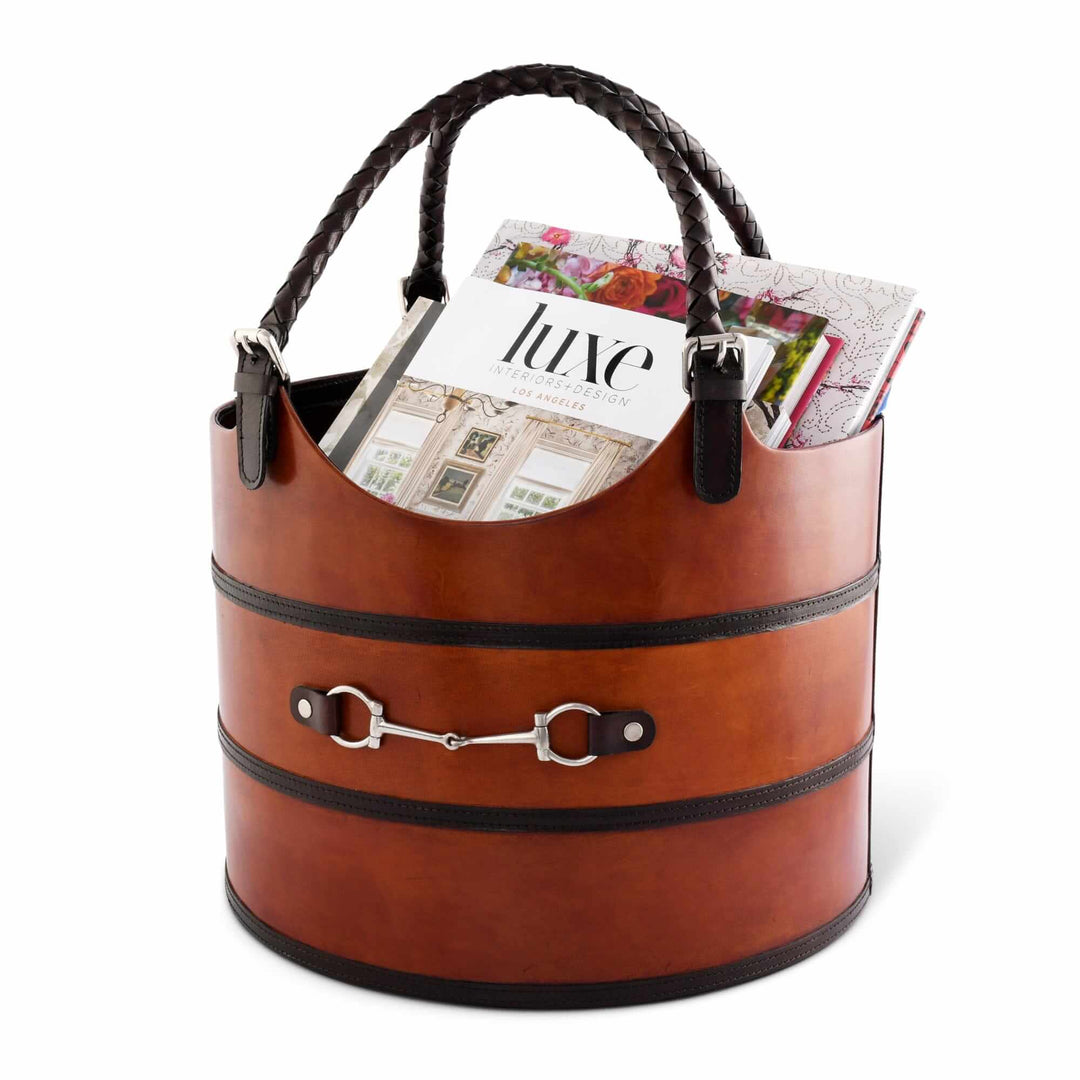 Brown leather basket with black trim holding magazines on a white background