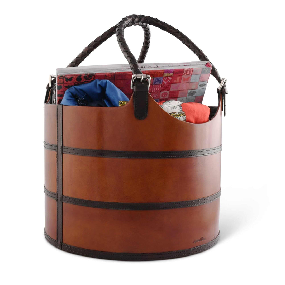 Brown leather magazine basket with handles filled with items on a white background