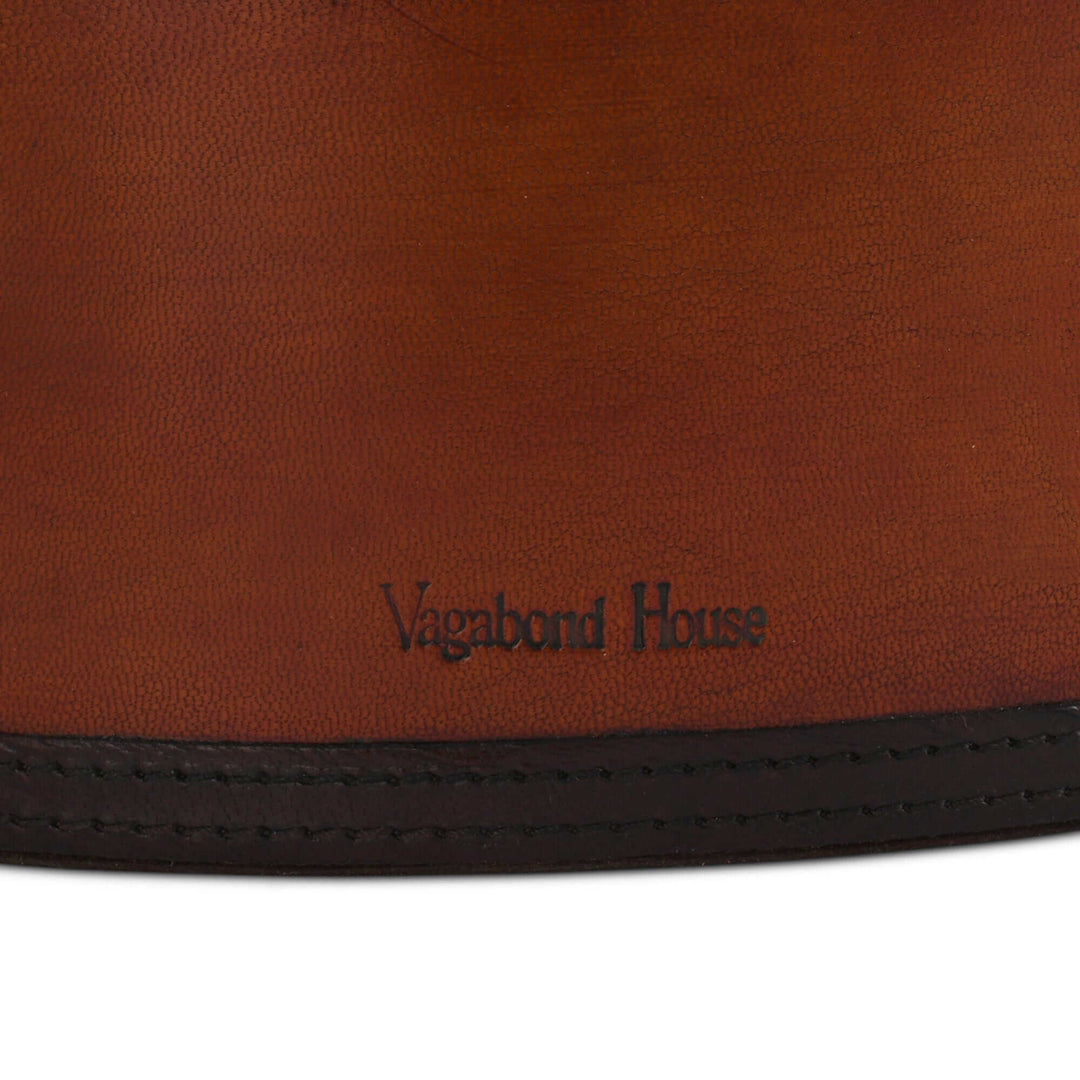 Close-up of a brown leather magazine basket with 'Vagabond House' branding.