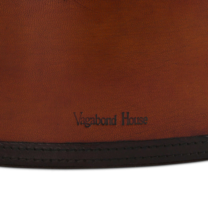 Close-up of a brown leather magazine basket with 'Vagabond House' branding.