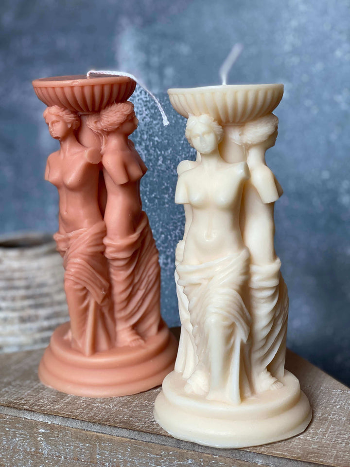 Two statuesque candle holders, one pink and one white, on a textured surface with a blue gradient background.