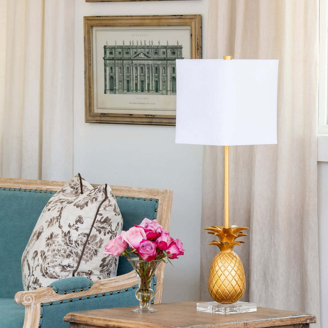 Decorative pineapple lamp on a side table with a floral arrangement and chair in a room.